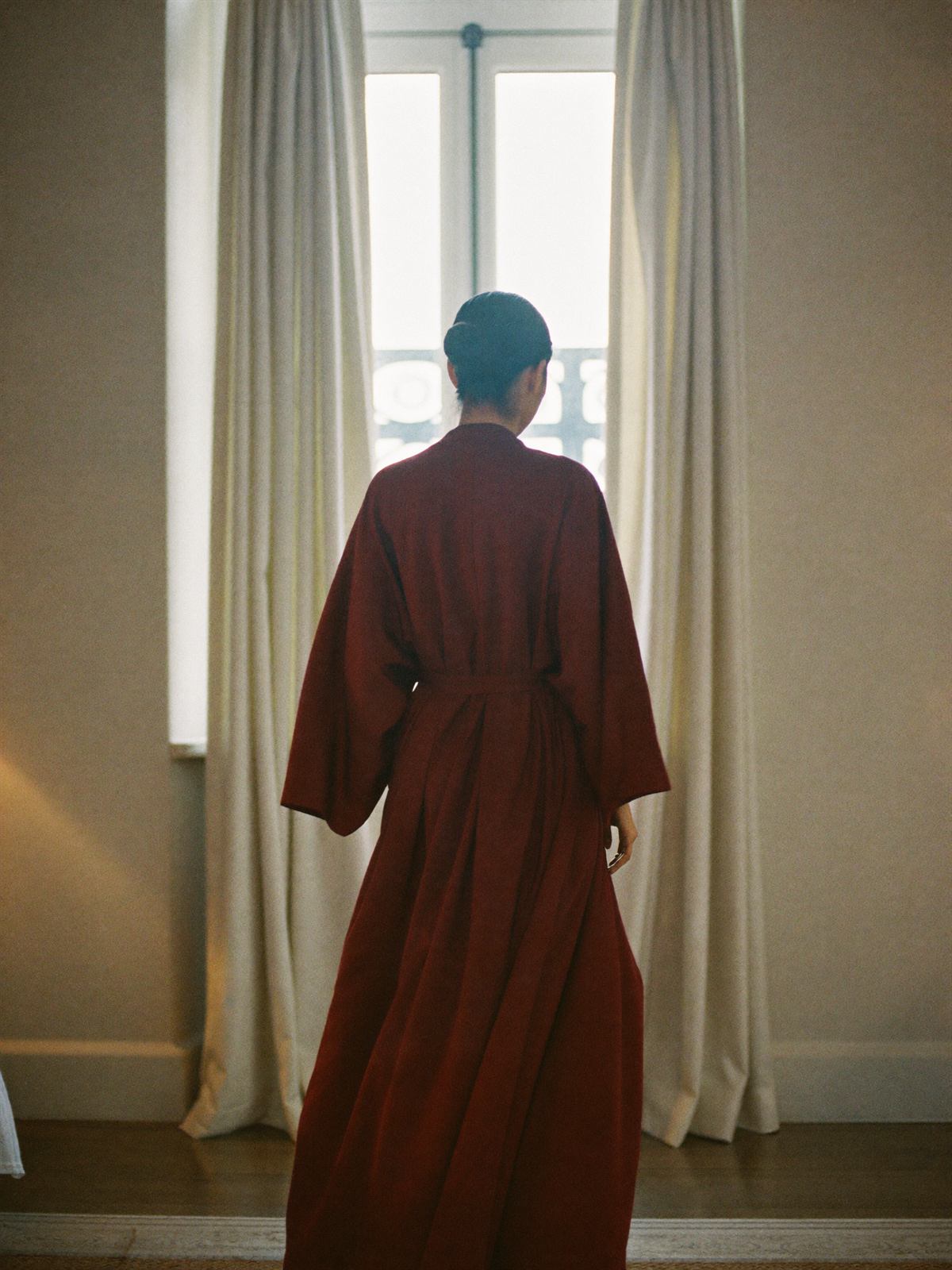 Woman in a long burgundy silk robe by a bright window