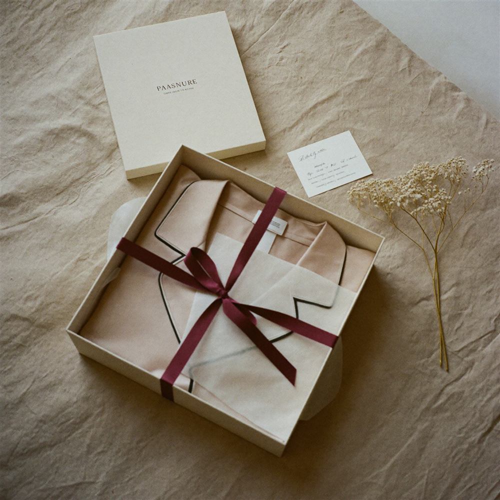 Ivory gift box with burgundy ribbon and silk pajamas in tissue