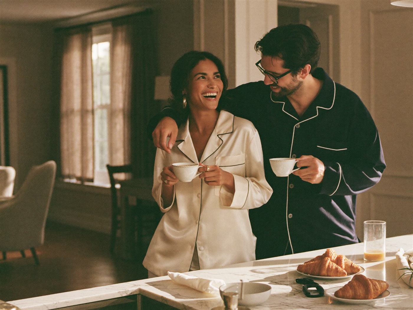 Couple in matching pajamas laughing over morning coffee